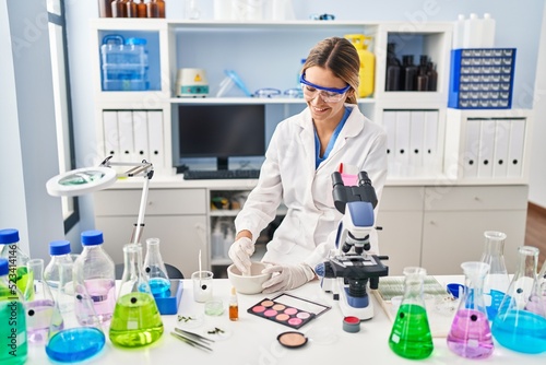 Young hispanic woman scientist making makeup working at laboratory