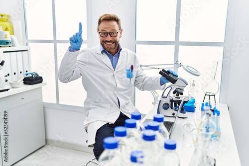 Middle age man working at scientist laboratory smiling with an idea or question pointing finger with happy face  number one