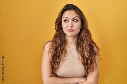 Young hispanic woman standing over yellow background smiling looking to the side and staring away thinking.