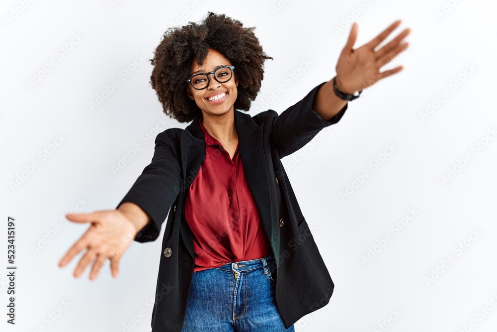 African american woman with afro hair wearing business jacket and glasses looking at the camera smiling with open arms for hug. cheerful expression embracing happiness. African american woman with afro hair wearing business jacket and glasses looking at the camera smiling with open arms for hug. cheerful expression embracing happiness.