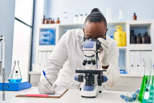 Young african american man wearing scientist uniform using microscope at laboratory