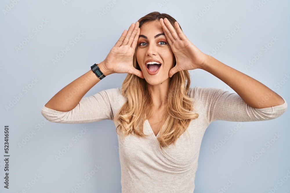 Fototapeta premium Young blonde woman standing over isolated background smiling cheerful playing peek a boo with hands showing face. surprised and exited
