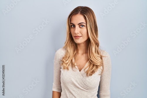Young blonde woman standing over isolated background relaxed with serious expression on face. simple and natural looking at the camera.