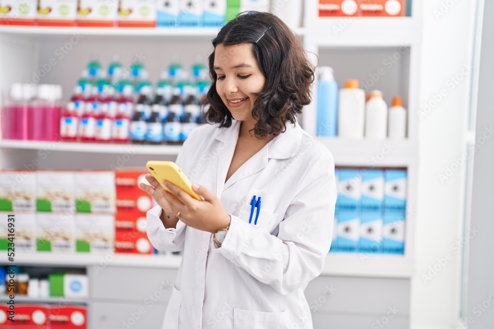 Young woman pharmacist using smartphone working at pharmacy