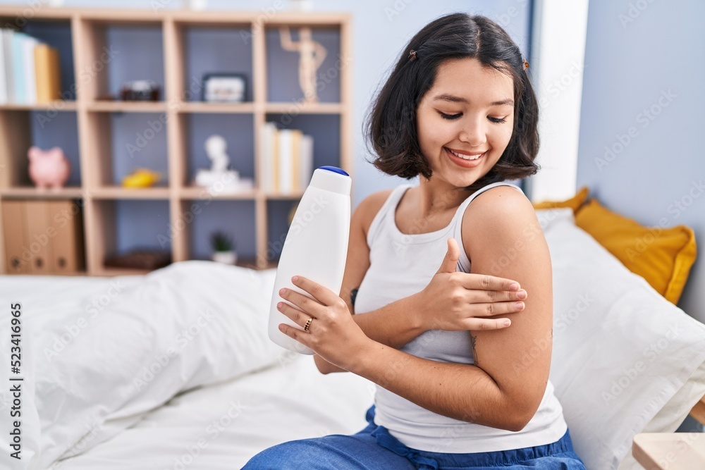 Young woman applying lotion on arm sitting on bed at bedroom Young woman applying lotion on arm sitting on bed at bedroom