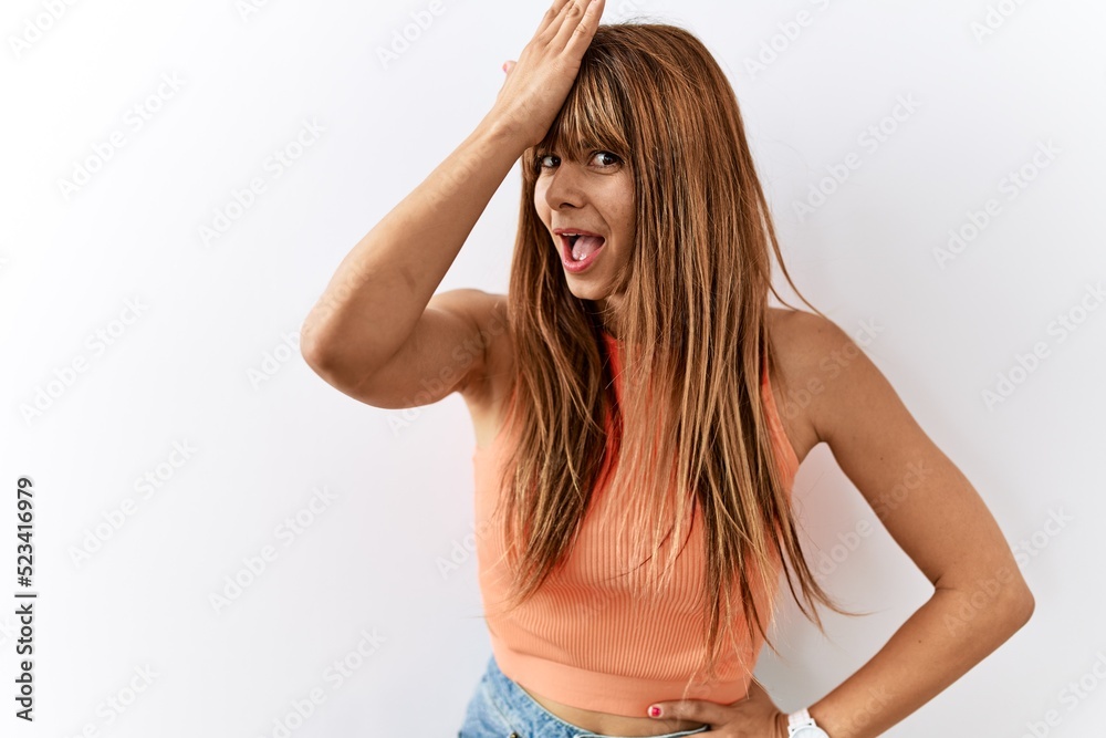 Hispanic woman with bang hairstyle standing over isolated background surprised with hand on head for mistake, remember error. forgot, bad memory concept. Hispanic woman with bang hairstyle standing over isolated background surprised with hand on head for mistake, remember error. forgot, bad memory concept.