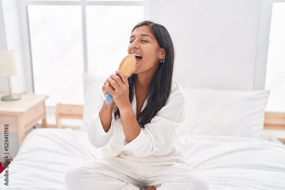 Young beautiful hispanic woman singing song using brush as a microphone at bedroom Young beautiful hispanic woman singing song using brush as a microphone at bedroom