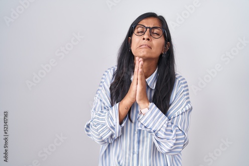 Young hispanic woman wearing glasses begging and praying with hands together with hope expression on face very emotional and worried. begging. © Krakenimages.com