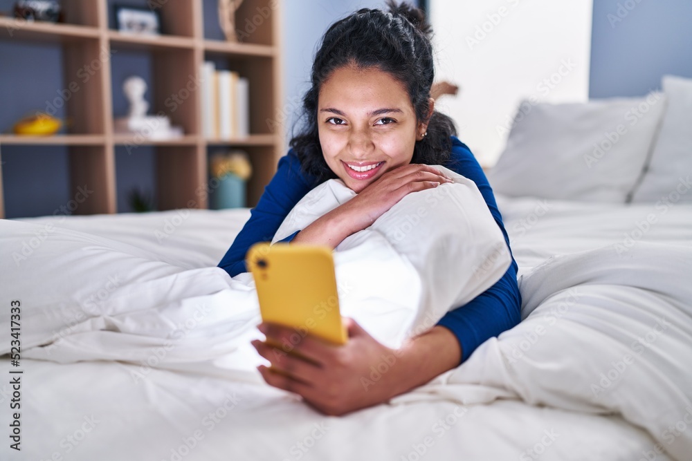 Young latin woman using smartphone lying on bed at bedroom Young latin woman using smartphone lying on bed at bedroom