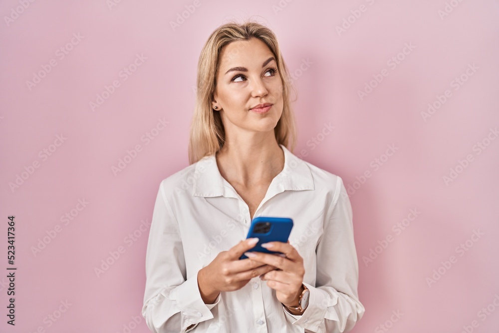 Young caucasian woman using smartphone typing message smiling looking to the side and staring away thinking. Young caucasian woman using smartphone typing message smiling looking to the side and staring away thinking.