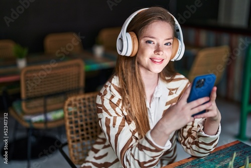 Young caucasian woman listening to music sitting on table at restaurant