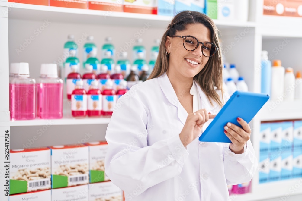 Young hispanic woman pharmacist smiling confident using touchpad at pharmacy