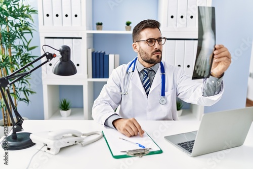 Young hispanic man wearing doctor uniform looking xray at clinic