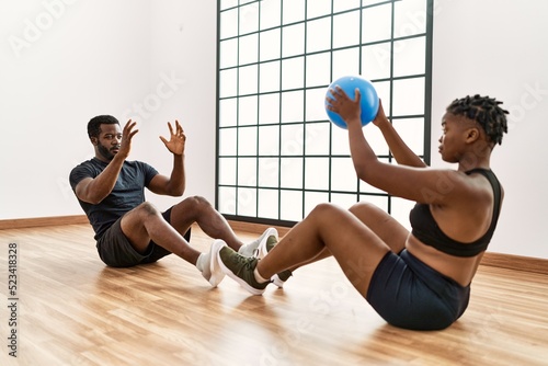 Young african american sporty couple doing abs exercise using ball at sport center.