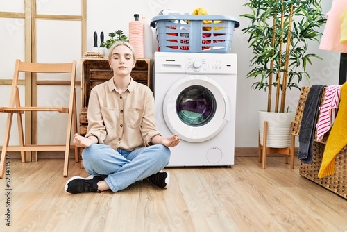 Young caucasian woman doing yoga waiting for washing machine at laundry room