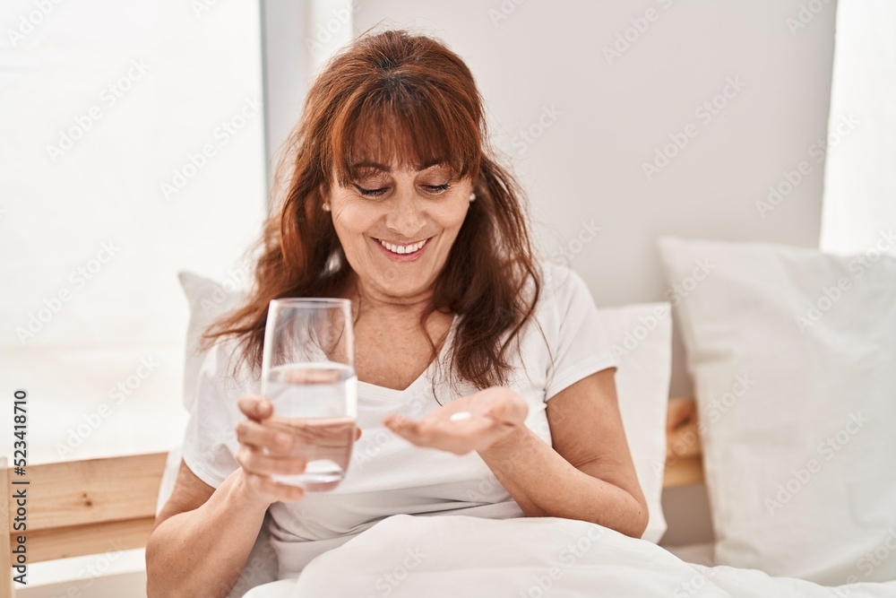 Middle age woman taking pill sitting on bed at bedroom Middle age woman taking pill sitting on bed at bedroom
