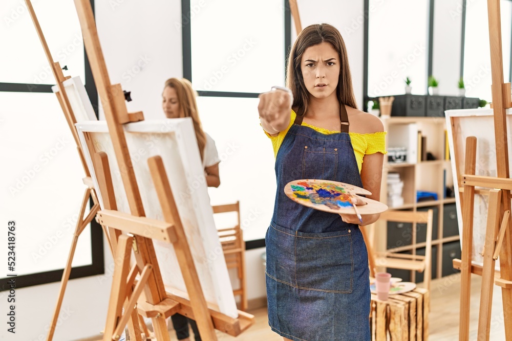 Young hispanic woman at art classroom pointing with finger to the camera and to you, confident gesture looking serious Young hispanic woman at art classroom pointing with finger to the camera and to you, confident gesture looking serious