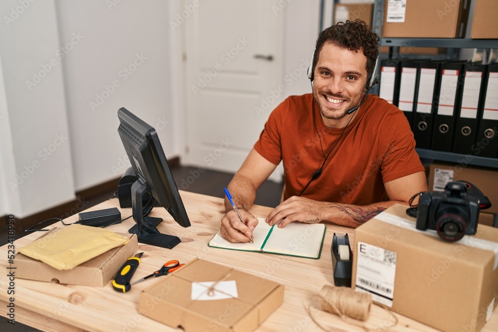 Young hispanic man ecommerce call center agent having video call writing on notebook at office Young hispanic man ecommerce call center agent having video call writing on notebook at office