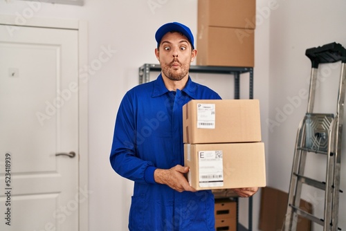 Young hispanic man working on moving service holding boxes making fish face with mouth and squinting eyes, crazy and comical. © Krakenimages.com