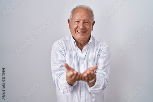 Senior man with grey hair standing over isolated background smiling with hands palms together receiving or giving gesture. hold and protection