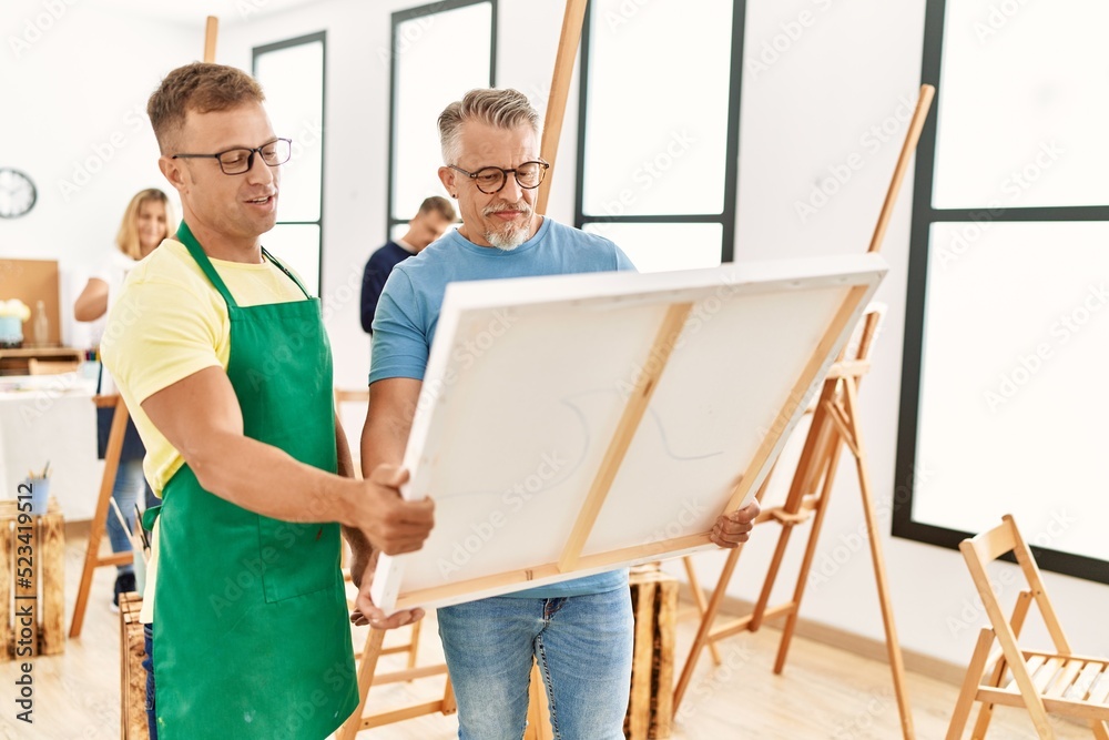 Group of middle age people drawing at art studio. Two students smiling happy holding canvas.