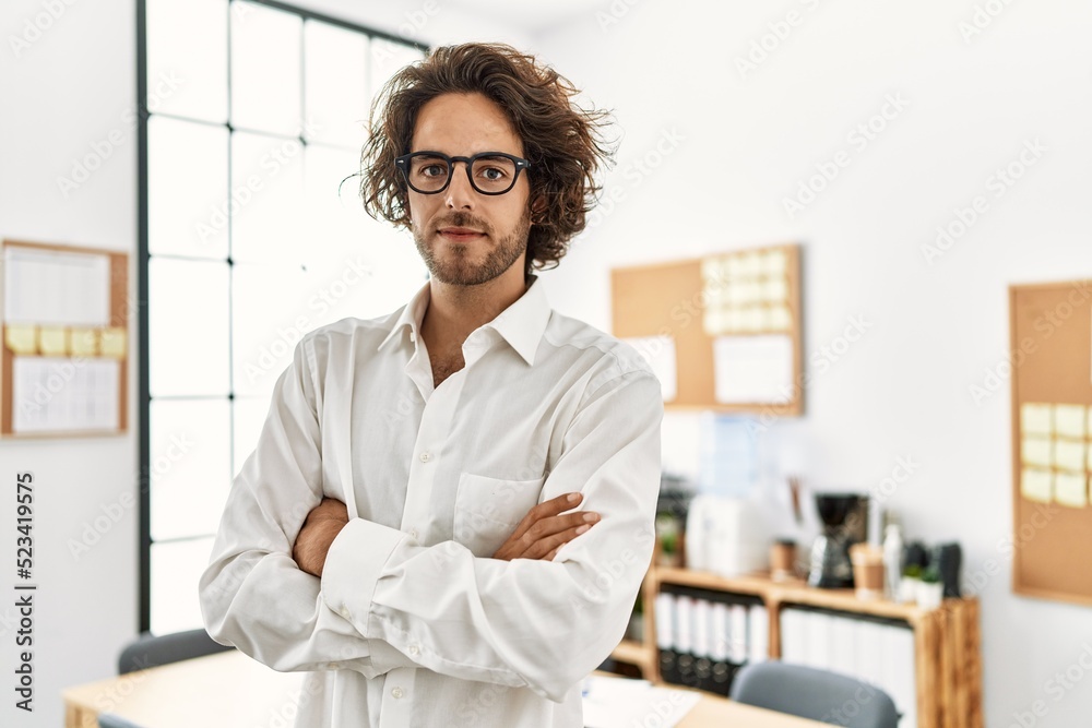 Young hispanic businessman with serious expression standing with arms crossed gesture at office.
