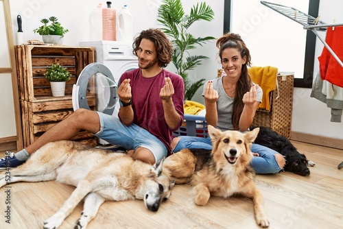 Photography Young hispanic couple doing laundry with dogs doing money gesture with hands, as