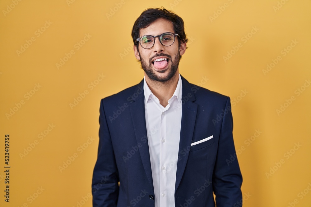 Handsome latin man standing over yellow background sticking tongue out happy with funny expression. emotion concept. Handsome latin man standing over yellow background sticking tongue out happy with funny expression. emotion concept.