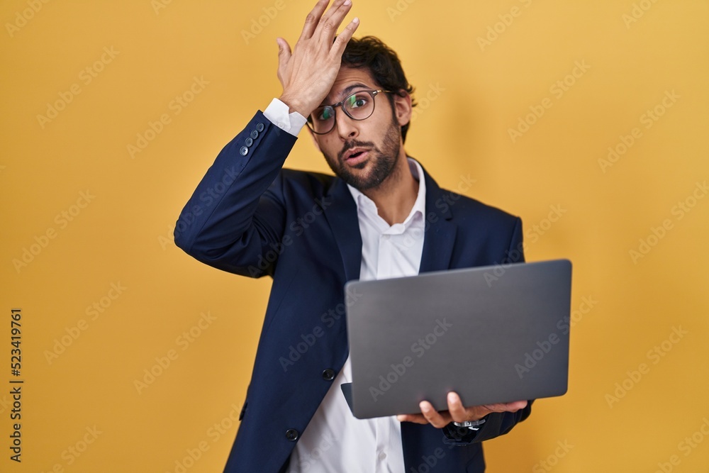 Handsome latin man working using computer laptop surprised with hand on head for mistake, remember error. forgot, bad memory concept.