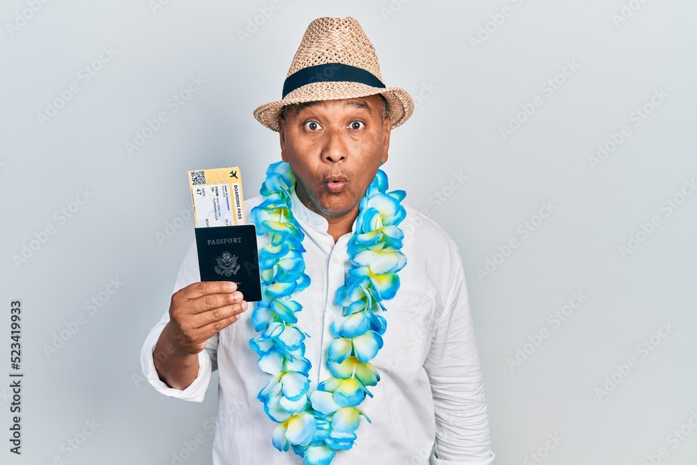 Middle age latin man wearing summer style holding boarding pass and passport scared and amazed with open mouth for surprise, disbelief face Middle age latin man wearing summer style holding boarding pass and passport scared and amazed with open mouth for surprise, disbelief face