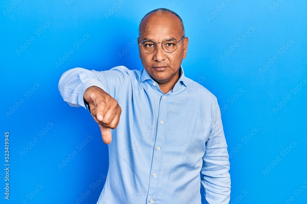 Middle age latin man wearing casual clothes and glasses looking unhappy and angry showing rejection and negative with thumbs down gesture. bad expression.