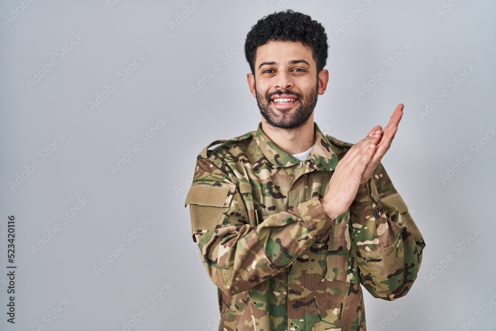 Arab man wearing camouflage army uniform clapping and applauding happy and joyful, smiling proud hands together
