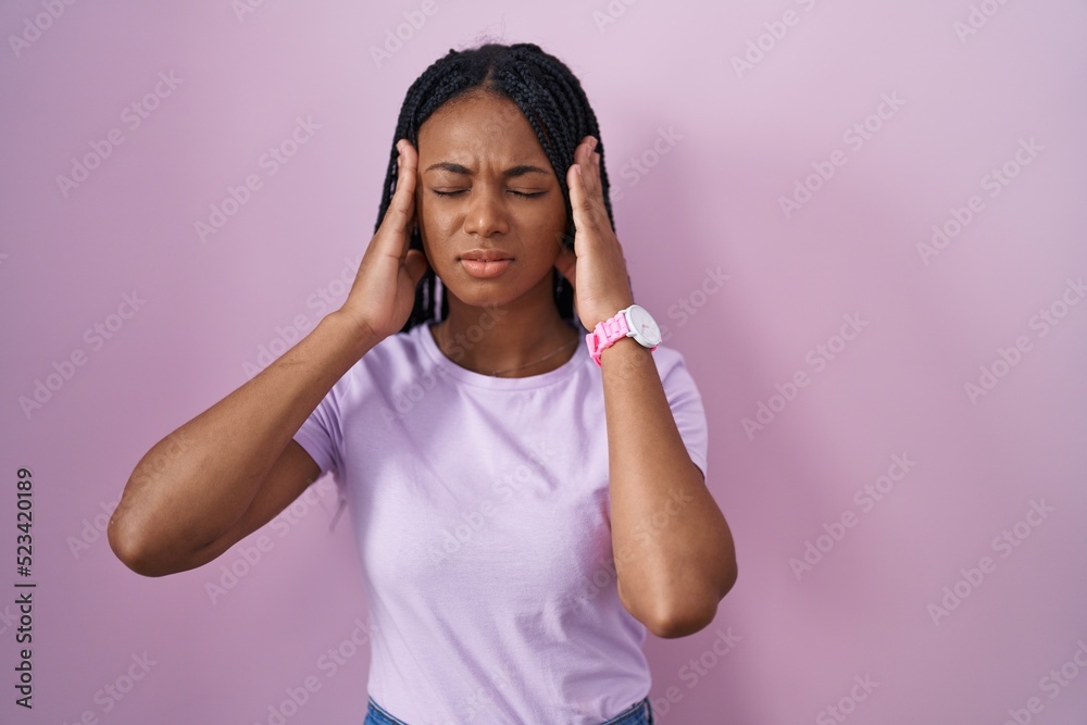 African american woman with braids standing over pink background with hand on head, headache because stress. suffering migraine. African american woman with braids standing over pink background with hand on head, headache because stress. suffering migraine.