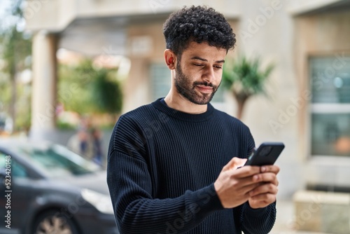Young arab man smiling confident using smartphone at street