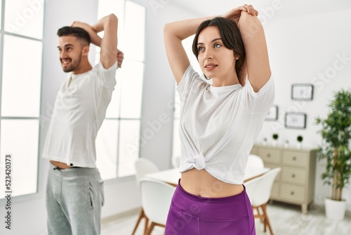 Young hispanic couple doing sport streching arms at home