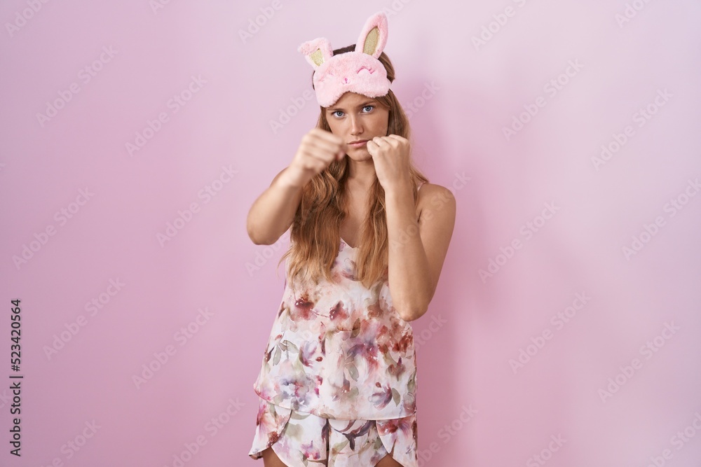 Young caucasian woman wearing sleep mask and pajama punching fist to fight, aggressive and angry attack, threat and violence Young caucasian woman wearing sleep mask and pajama punching fist to fight, aggressive and angry attack, threat and violence
