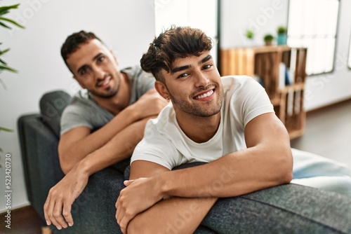 Two hispanic men couple smiling confident sitting on sofa at home