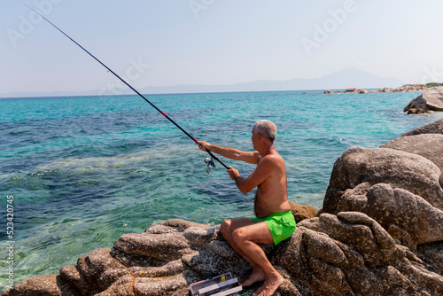 Fisherman sitting on a rock and fishing with a rod