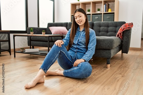 Young chinese girl smiling happy sitting on the floor at home.