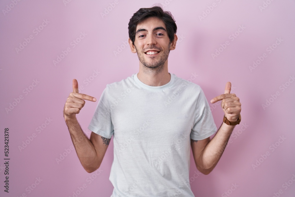 Young hispanic man standing over pink background looking confident with smile on face, pointing oneself with fingers proud and happy. Young hispanic man standing over pink background looking confident with smile on face, pointing oneself with fingers proud and happy.