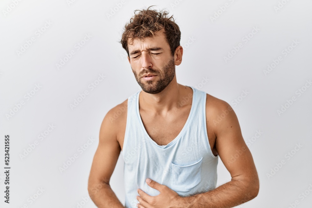 Young handsome man standing over isolated background with hand on stomach because nausea, painful disease feeling unwell. ache concept. Young handsome man standing over isolated background with hand on stomach because nausea, painful disease feeling unwell. ache concept.