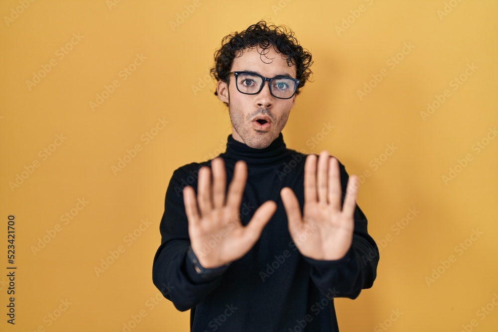 Fototapeta premium Hispanic man standing over yellow background moving away hands palms showing refusal and denial with afraid and disgusting expression. stop and forbidden.