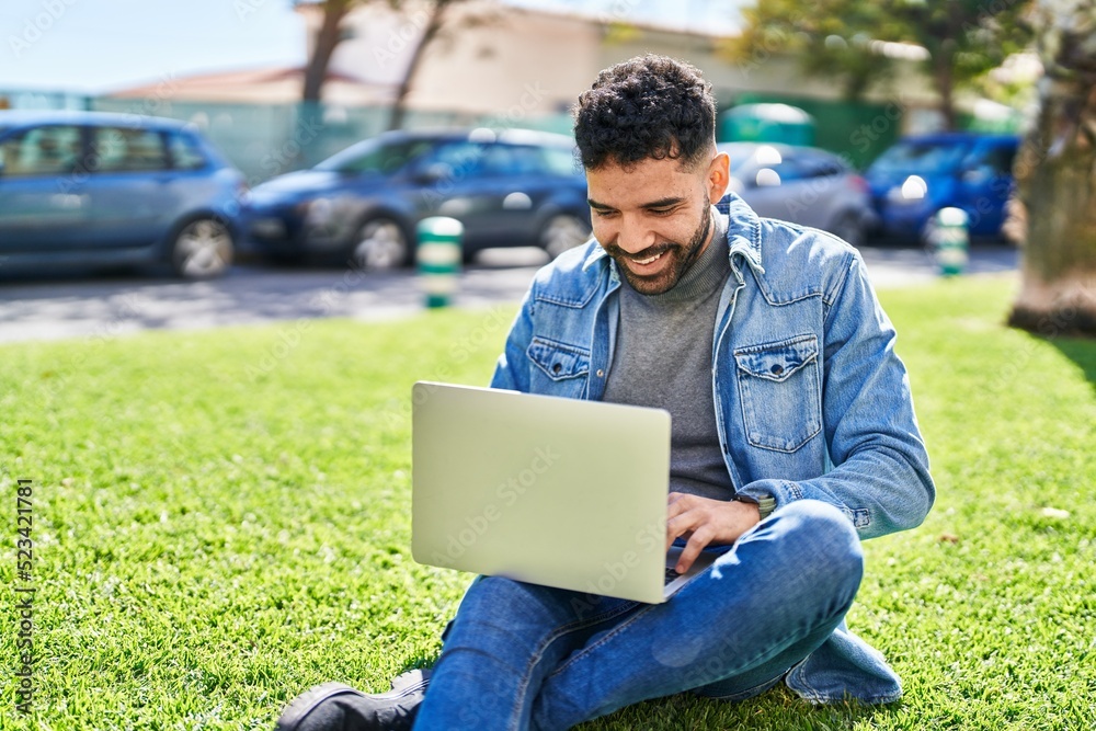 Young hispanic man using laptop sitting on herb at park Young hispanic man using laptop sitting on herb at park