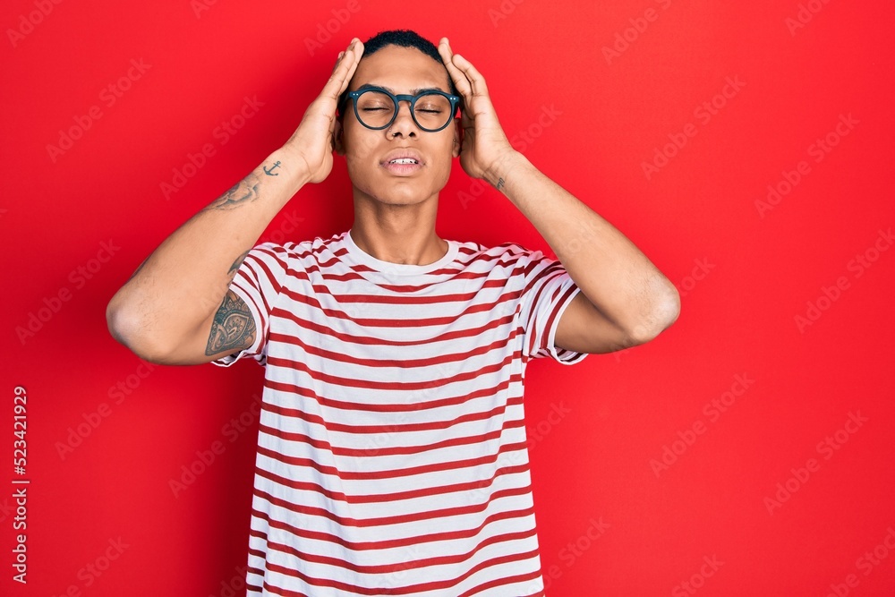 Young african american guy wearing casual clothes and glasses suffering from headache desperate and stressed because pain and migraine. hands on head. Young african american guy wearing casual clothes and glasses suffering from headache desperate and stressed because pain and migraine. hands on head.