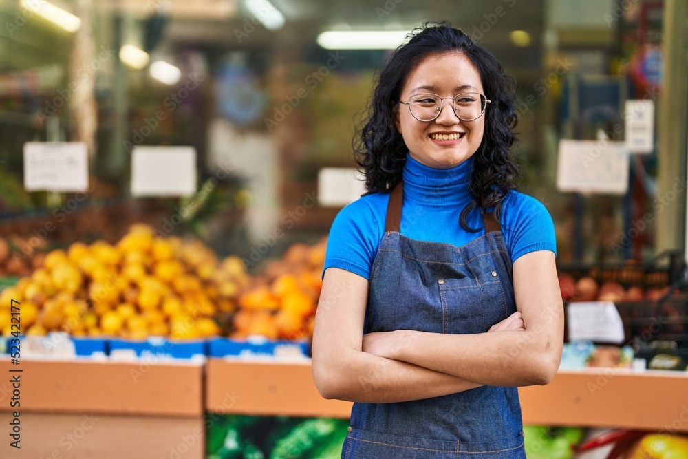 Young chinese woman employee smiling confident standing with arms crossed gesture at fruit store