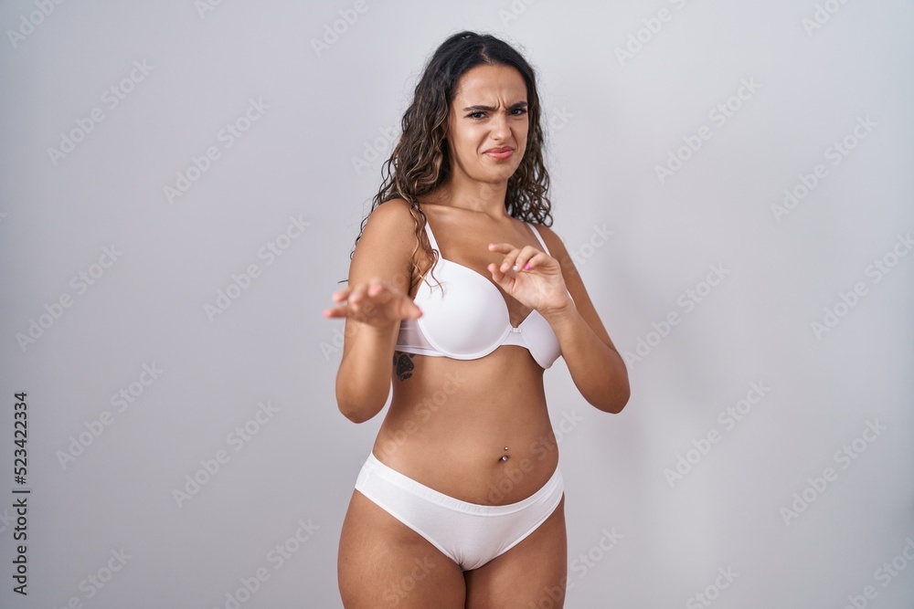 Fototapeta premium Young hispanic woman wearing white lingerie disgusted expression, displeased and fearful doing disgust face because aversion reaction.