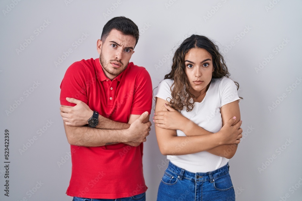 Young hispanic couple standing over isolated background shaking and freezing for winter cold with sad and shock expression on face Young hispanic couple standing over isolated background shaking and freezing for winter cold with sad and shock expression on face