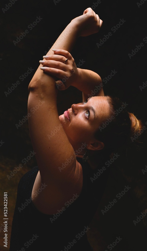 Mujer posando brazos hacia arriba y mirando al cielo de donde viene la luz con fondo negro Mujer posando brazos hacia arriba y mirando al cielo de donde viene la luz con fondo negro