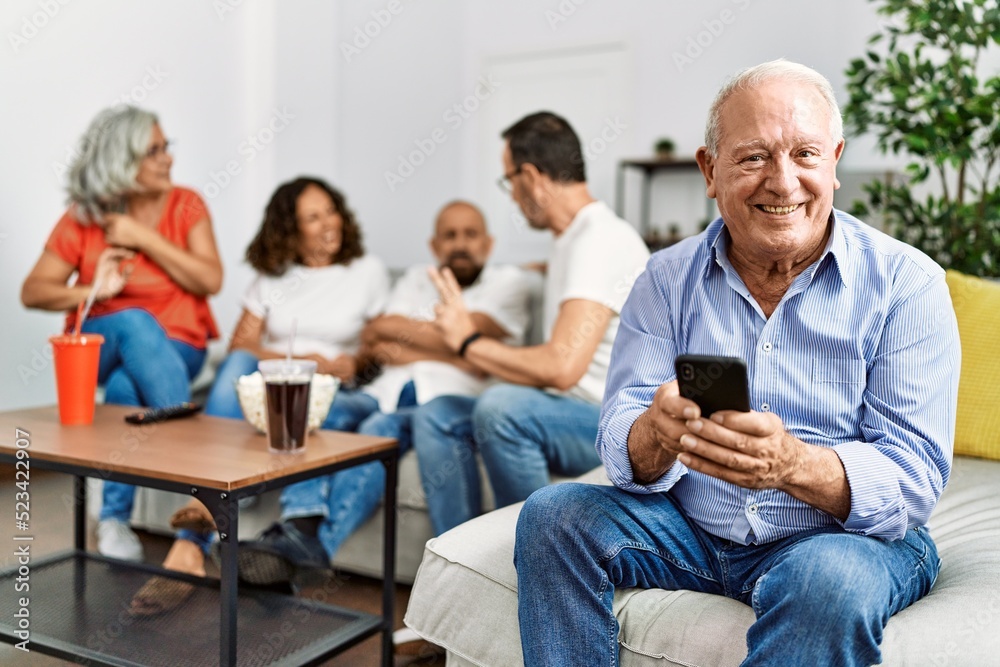Group of middle age friends sitting on the sofa speaking. Man smiling happy using smartphone at home. Group of middle age friends sitting on the sofa speaking. Man smiling happy using smartphone at home.