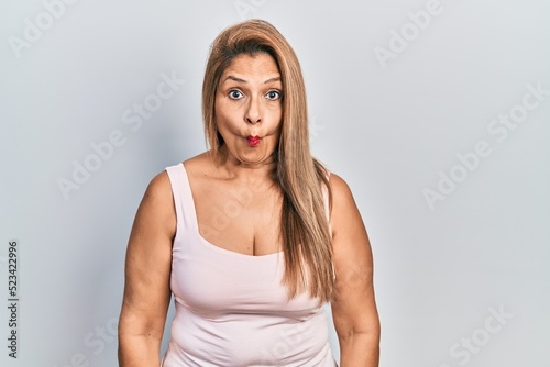 Middle age hispanic woman wearing casual style with sleeveless shirt making fish face with lips, crazy and comical gesture. funny expression.